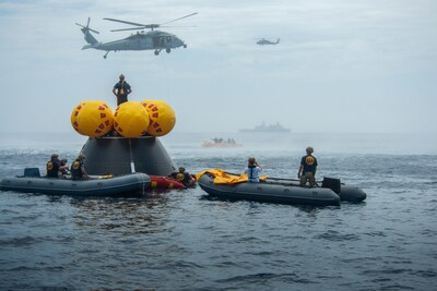 Naval helicopters fly over a test version of NASA's Orion spacecraft and personnel involved in training activities in the Pacific Ocean in July 2023, in preparation for Artemis II. Teams from NASA, including the Artemis II crew, and the Department of Defense are training this month off the coast of San Diego to prepare to recover the astronauts and Orion when they return to Earth. Credits: NASA/Kenny Allen