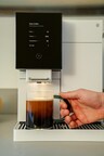 Closeup of white TK-02 with a drip coffee being brewed underneath the machine's spout. A hand is reaching to pick up the drink.
