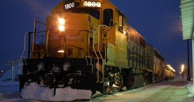 Ontario Northlander parked at a train station during twilight in a snowy setting. The locomotive's headlights and station lighting cast a warm glow on the surrounding area, contrasting with the blue hues of the early evening sky. (CNW Group/Unifor)