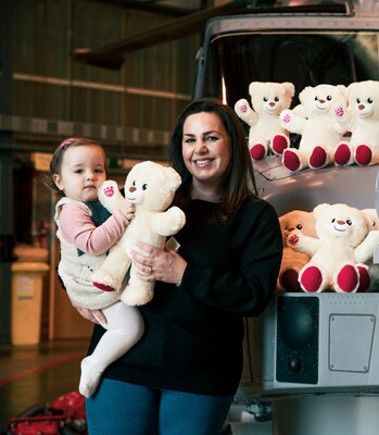 A military mother and child smile with donated Build-A-Bear furry friends at a Royal Naval Air Station. Since 2020, Build-A-Bear Foundation has partnered with Little Troopers to provide comforting teddy bears for military children missing a serving parent.