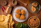 Golden coxinhas on a rack, one opened on a plate showing its chicken filling, with a bowl of filling, PERFEITO NO.2 seasoning, chili peppers, and parsley on a wood table.