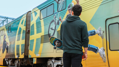 A person with a skateboard standing next to the Amtrak Pacific Surfliner train.