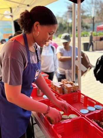 Student LunchBox volunteer is replenishing food in the red baskets for other students to receive