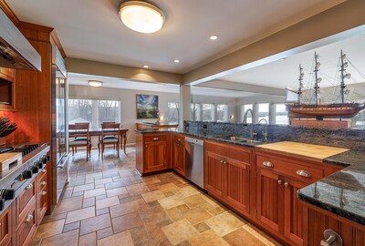 A lovely kitchen sits at the center of the main residence, and enjoys views of the river thanks to a wall of windows on the waterside of the home (partially shown). It is adjacent to an informal dining area and dry bar (left-of-center), family room with stone fireplace, formal dining, butler's pantry and office. MaineLuxuryAuction.com.