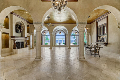 Upon entering the residence, one is greeted by the elegant, grand salon on the main living level. Hand-carved columns and a stone fireplace enjoy the backdrop provided by sublime lake views via a row of floor-to-ceiling windows. LakefrontLuxuryAuction.com.