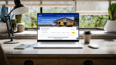 Penske's new commercial rental website for businesses showcased on a laptop computer on a window facing desk with a blue sky and green leady trees.
