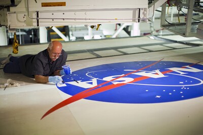 In Orbiter Processing Facility-2 at NASA’s Kennedy Space Center in Florida, Michael Williams of United Space Alliance paints the NASA logo — known as the “meatball” — on the left wing of space shuttle Endeavour in 2012. Credit: NASA/Dimitri Gerondidakis