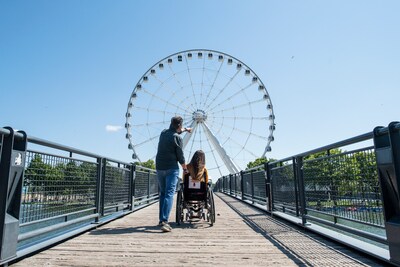 Un homme pointant la grande roue de Montréal et une femme en situation de handicap admirant l'attrait touristique.  Crédit photo : Gaëlle Leroyer (Groupe CNW/Kéroul)