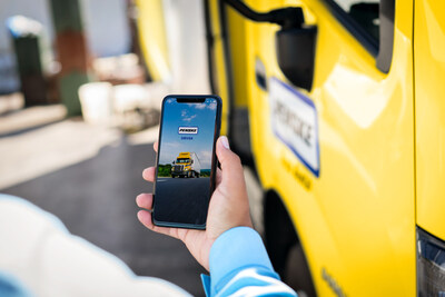 Hand holding mobile phone with Penske Driver on screen in front of yellow Penske-branded truck