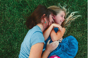 Mother and daughter laughing while laying in the grass.