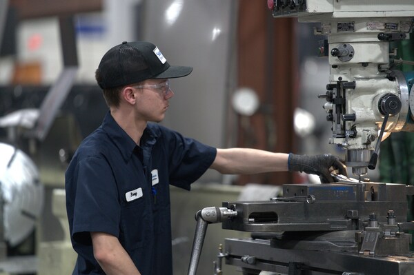 Young man operating a lath machine in a factory.