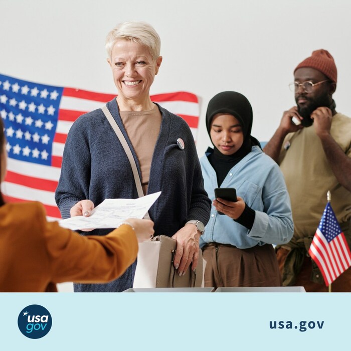 “A woman smiles handing her ballot to a poll worker at a table while two other people wait in line to vote above a footer with the USAGov logo and the usa.gov URL”