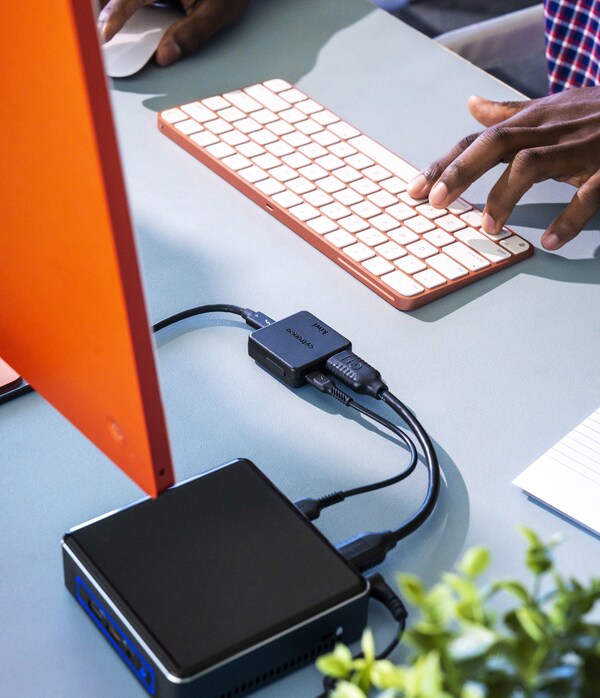 A desktop setup showing a keyboard, partial monitor view, and hands using a mouse and keyboard to operate a host computer. The Kiwi device connects the host to a target mini-PC, demonstrating seamless control of the target device through Cytrence Kiwi's compact design and clean connectivity.