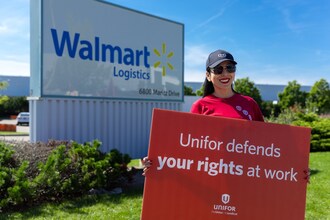 Walmart worker outside of company warehouse holding a sign that reads 'Unifor defends your rights at work'. (CNW Group/Unifor)