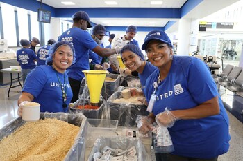 United Airlines employees smile for a photo while packaging meals with nonprofit Rise Against Hunger at Newark Liberty International Airport (EWR).