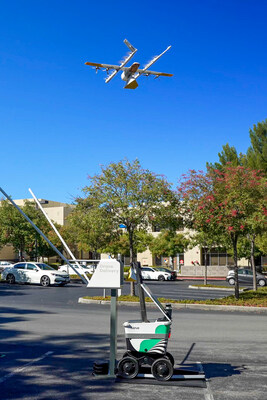 A Wing drone hovers at the AutoLoader, where it will pick up a delivery from a Serve robot for aerial delivery.