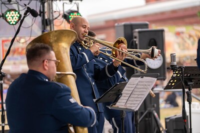 Two brass musicians in the US Air Force Band of the Golden West brass quintet, Travis Brass, play with plunger mutes during a live outdoor performance.