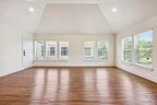 Spacious living room in a second-floor Marquita Court apartment, boasting natural light from large windows, vaulted ceilings, recessed lighting, and new hardwood flooring