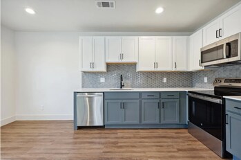 Modern kitchen in a Marquita Court studio apartment, featuring two-tone designer cabinetry, stainless steel appliances, quartz countertops, and era-inspired backsplash tile.