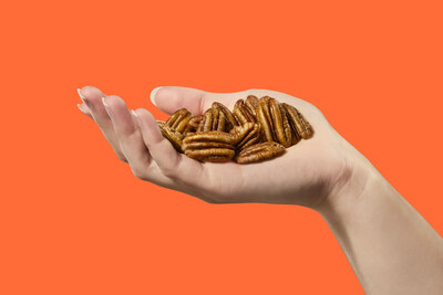 A hand holding pecans on an orange background