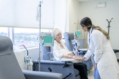 A senior woman is sitting on a chair in a chemotherapy treatment room. She is wearing a headscarf due to hair loss. Her female oncologist is checking in on her and providing her with moral encouragement.