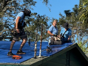 Hope Force International Reservists secure tarp to a roof of a home damaged by Hurricane Milton. Tarps protect homes from further damage from rain and other elements.