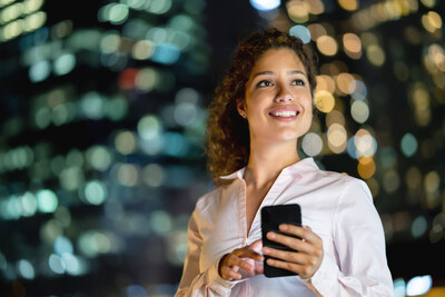 Portrait of a business woman working at night using her cell phone and smiling.