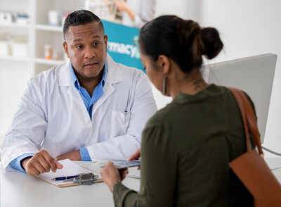 Female pharmacy customer asks a male pharmacist questions about the flu vaccine. She is reading an informational flyer.