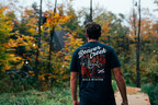 Model wearing Bold Aviator Beaver Creek Tee standing in front of the Beaver Creek Maine A-Frame Cabin