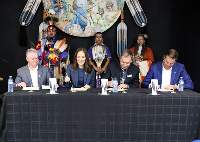 From the unceded and traditional Tk’emlúps te Secwépemc territory, BMO and All Nations Trust Company sign agreement to partner in BC. Pictured back row, the Sage Hill Dancers. Pictured seated front row L-R:  Tim Low (ANTCO), Clio Straram (BMO) Pat Fosbery (ANTCO) and Greg Vriend (BMO). Art by Raven Dave Seymour. Photo credit: Melissa Mongrain (CNW Group/BMO Financial Group)