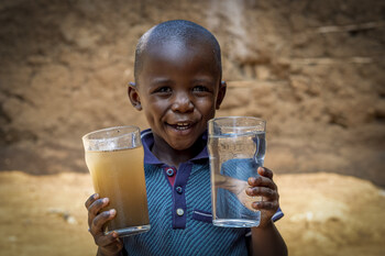 A young boy living in Kibera holds a glass of pre-filtered water and a glass of clean, safe drinking water created by the Sawyer PointONE filter distributed by The Bucket Ministry.