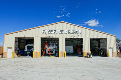 A large garage building with a sign that reads "RV Service & Repair" and four open garage bay doors. Through the open doors RVs and a ladder are visible.