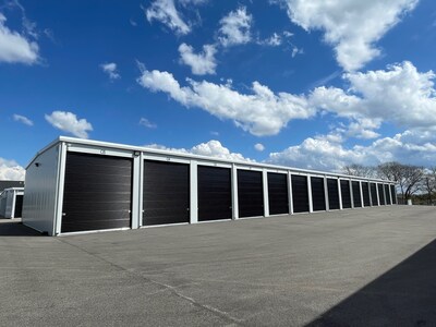 A row of large enclosed storage units with roll up garage doors on an asphalt surface.