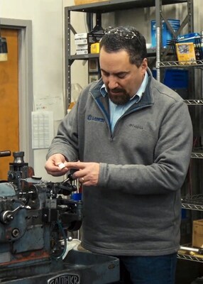 John Biagioni, president of Lampin, picks up a small metal component which has been manufacturered at Lampin, and points to a feature on the part.