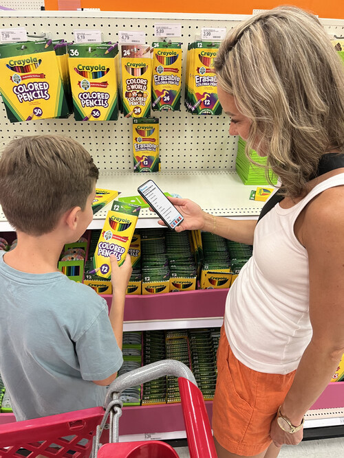 A mother uses TeacherLists on her phone while her son selects back-to-school supplies from his list. A mother uses TeacherLists on her phone while her son selects back-to-school supplies from his list.