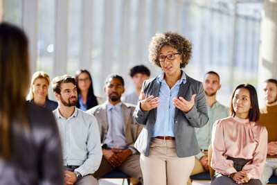 Mature female entrepreneur standing on education event in the office and talking to a presenter.