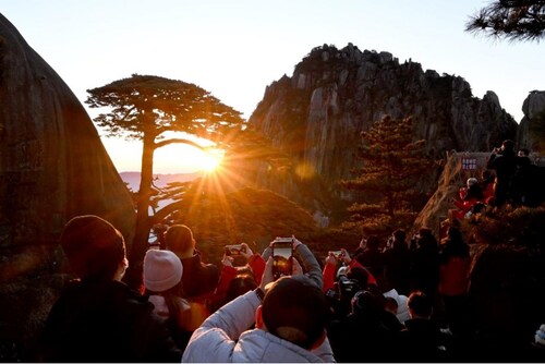 Wisatawan menikmati matahari terbit di lokasi wisata Huangshan, di bawah pohon "Sang Pinus Penyambut" – Xinhua/Huang Bohan (PRNewsfoto/The 2025 World Manufacturing Convention)