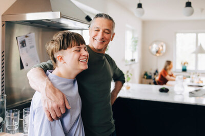 A dad with his arm around his son who has a disability, with the mom in the background on a laptop. (CNW Group/The Empire Life Insurance Company)