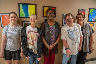 NEDHSA and Families Helping Families of NELA clients standing in front of their artworks on display next to the Phoenix Clinic signage.
