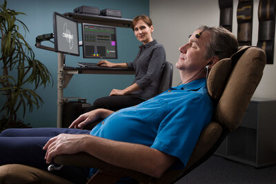 A female tech coach overseeing a male client relaxing in a zero-gravity chair while experiencing the BrainEcho™ process from Cereset®.