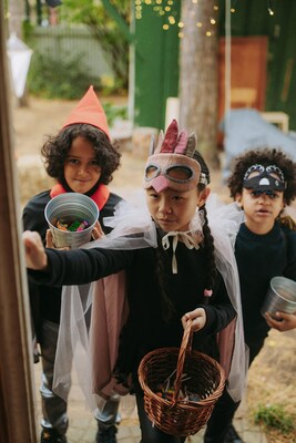 Three young children wearing costumes and holding buckets filled with candy are outside trick-or-treating.