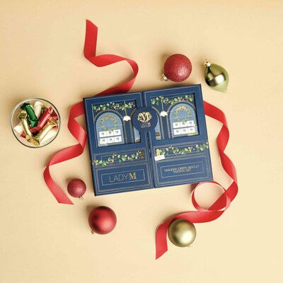 Top down view of Lady M's Holiday Crepe Biscuit Tasting Set on a beige background with red ribbon and ornaments.