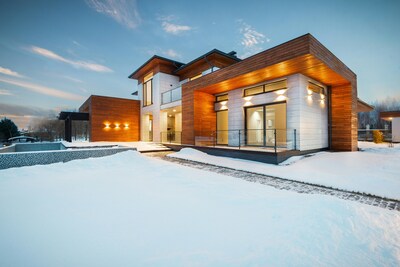 Modern house with its exterior lights on and snow in the front yard.