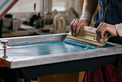Close-up of a screen printer pulling teal ink across a mesh screen using a squeegee during the apparel printing process.