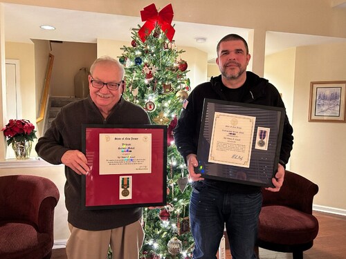 Vietnam veteran James Lamb and Eric Crafton stand before a Christmas tree, each holding a state service medal following a surprise ceremony honoring his service and resilience.