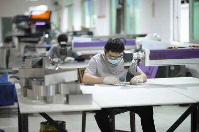 In LC Sign's precision manufacturing workshop, a technician uses a professional magnifying device to focus on the delicate assembly and calibration of signage components. Metal modules ready for processing are neatly arranged on the table, with other technicians working in the background, demonstrating the refined and standardized production enabled by the MaaS model.