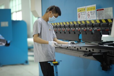 A worker operates a large CNC bending machine to precisely bend metal sheets. The prominent safety warning labels on the equipment and the protective gear worn by the worker reflect the factory's strict safety management standards, showcasing LC Sign's ability to achieve efficient, large-scale production through advanced industrial equipment under its MaaS model.