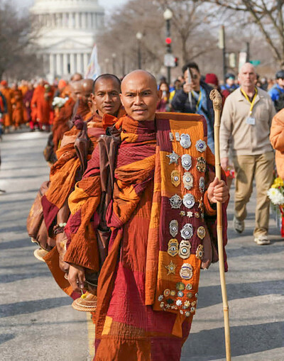 Protected Passage: A monk walks the final mile adorned with badges gifted by police and fire departments from across the country. These tokens were presented by local first responders who escorted the group through their towns, symbolizing a chain of protection that spanned 2,300 miles.