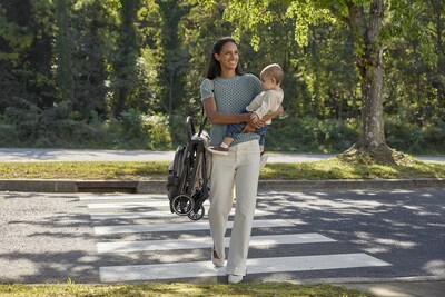 Parent carries her child while holding a compact, folded Britax Juniper+ stroller, demonstrating convenient portability and easy transport for everyday outings.