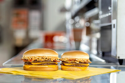 The Whataburger Bacon Steakhouse Double. Two burgers, in the standard and Jr sizes sit on a counter, topped melted aged cheddar, smoky bacon, crispy fried onions and tangy steak sauce, set in a restaurant kitchen.